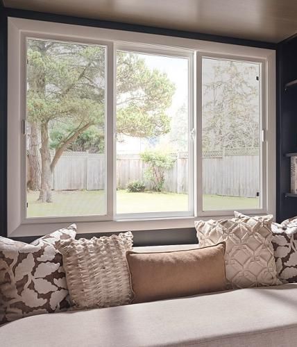 Wide three-panel horizontal slider window above a cushioned window seat overlooking a fenced yard