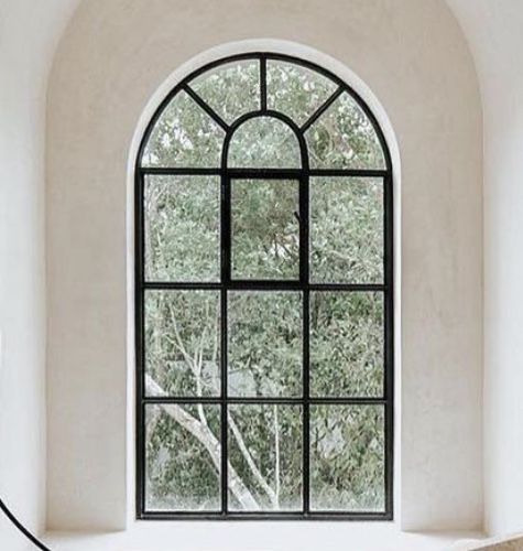 Tall arched geometric window with black grid bars set into a curved plaster wall