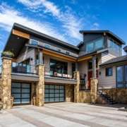 Modern luxury home with stone accents, expansive windows, covered balcony, and three-car garage