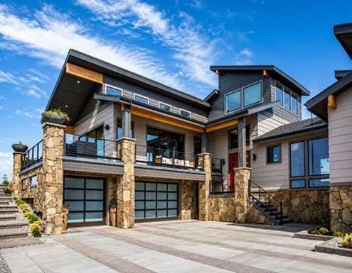 Modern luxury home with stone accents, expansive windows, covered balcony, and three-car garage