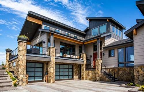 Modern luxury home with stone accents, expansive windows, covered balcony, and three-car garage