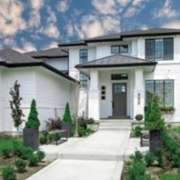 Modern white home with black metal roof, landscaped walkway, and manicured front lawn