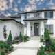 Modern white home with black metal roof, landscaped walkway, and manicured front lawn
