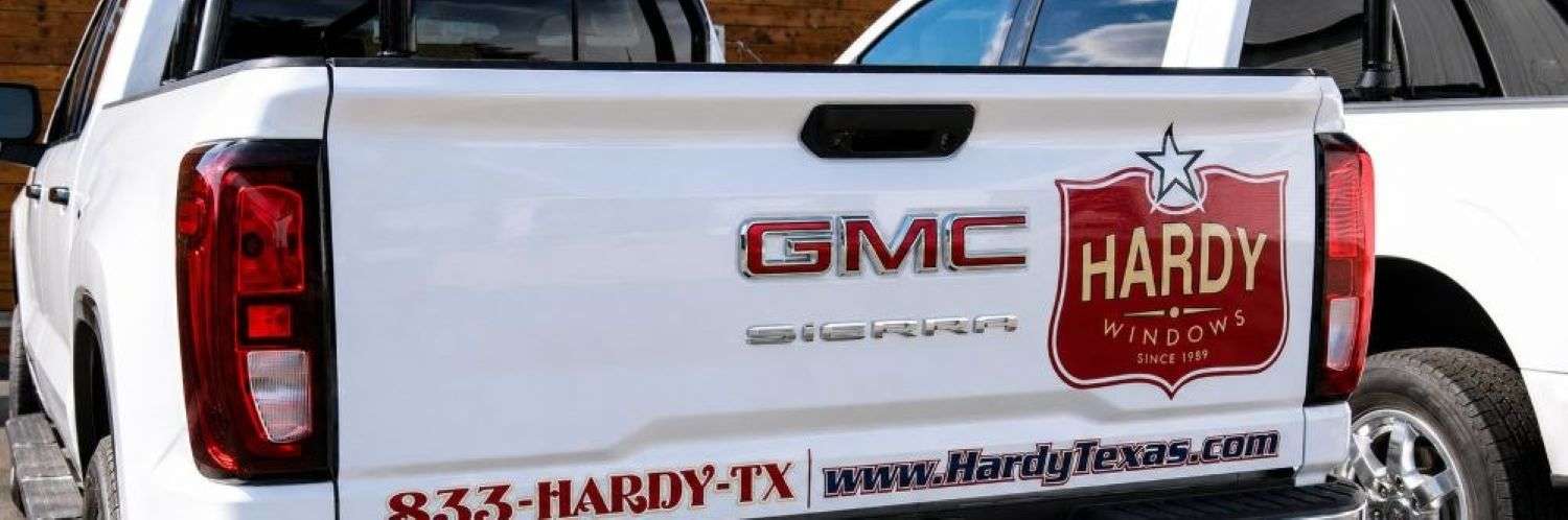 About Hardy Windows of Texas branded white GMC Sierra truck with company logo and website graphics on the tailgate.