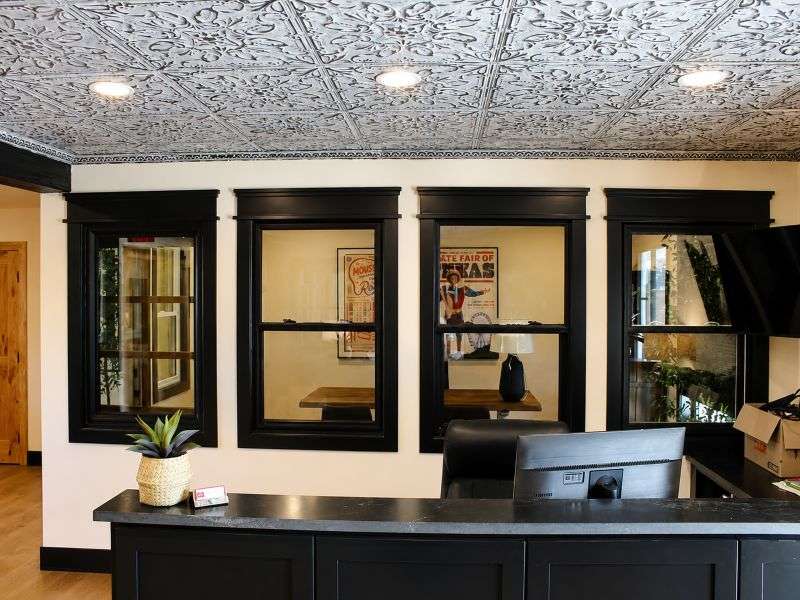 About Hardy Windows of Texas showroom with black-framed window displays, dark counter, wood floor, and ornate ceiling.