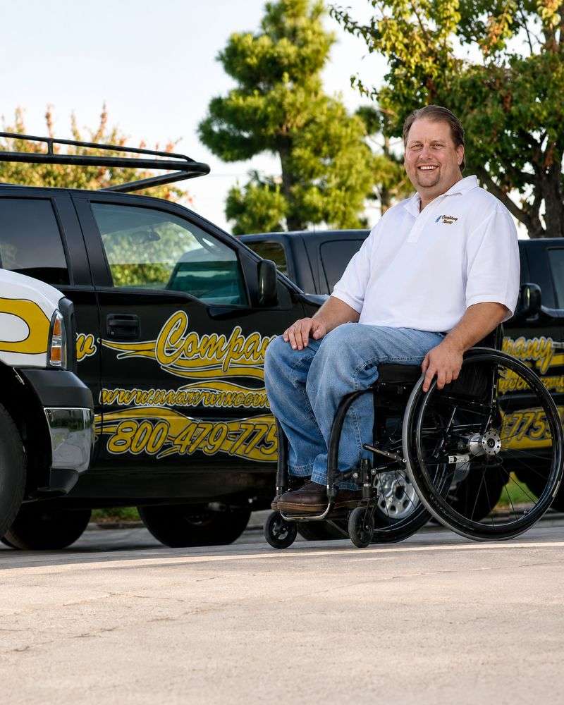 Hardy Windows founder Chance Hardy seated in his wheelchair beside two company branded service trucks