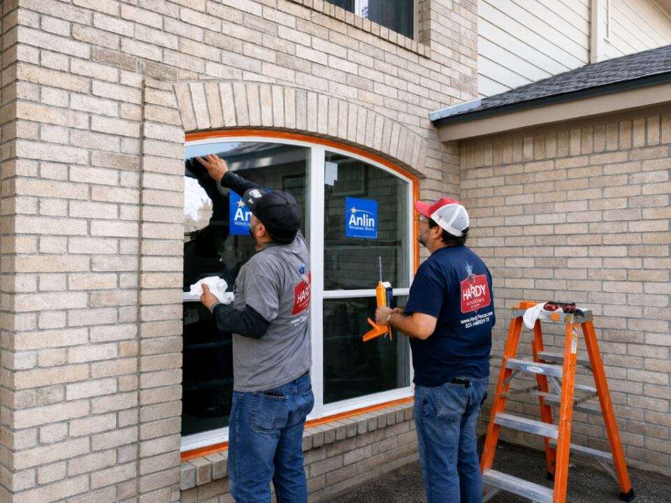 Two Hardy Windows of Texas installers fitting a new arched window into the brick exterior of a home